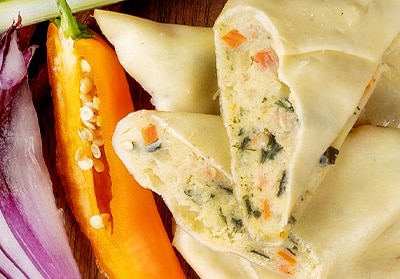 Angeschnittene Maultaschen in der Nahaufnahme mit Gemüsestücken in der Füllung, garniert mit einer angeschnittenen Paprika und einem Ziebelstreifen.