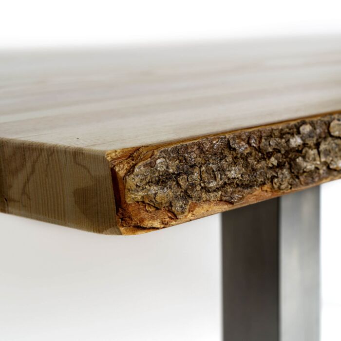 Auf diesem Detailbild ist eine Ecke der Massivholz-Tischplatte zu sehen. Hier wird der Übergang von glatt bearbeitetem Holz der schmalen Seite hin zur mit Baumrinde belassenen langen Seite sichtbar.