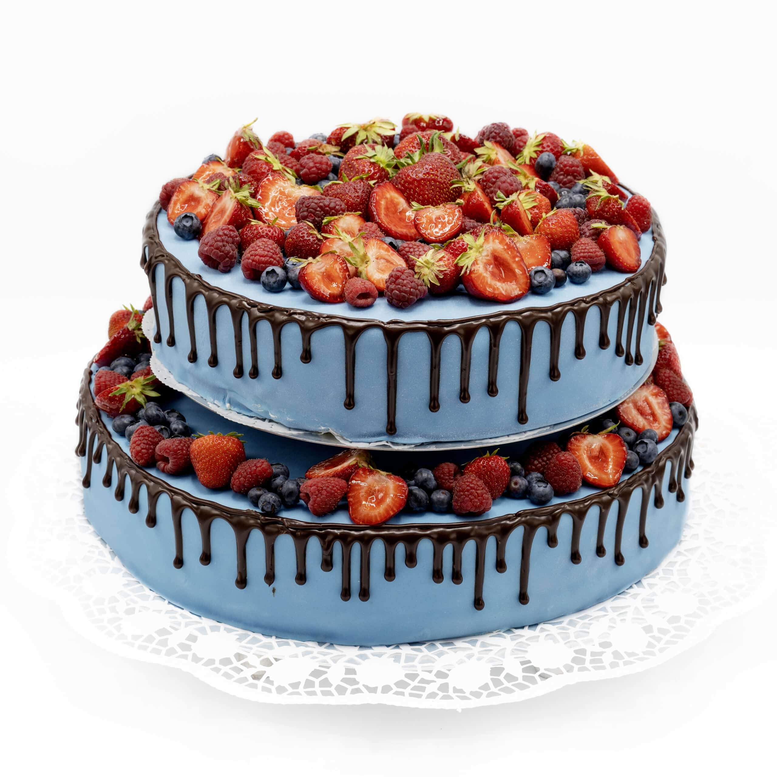 Eine zweistöckige Torte ist mit blauem Fondant überzogen. Am Rand laufen Schokoladen tropfen herunter. Zusätzlich sind beide ebenen mit frischen Beeren dekoriert.